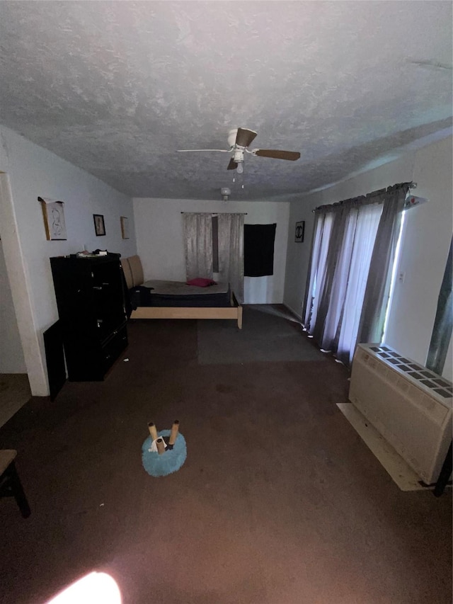 interior space featuring a textured ceiling, dark carpet, and ceiling fan