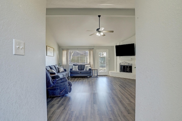 living room featuring beam ceiling, a brick fireplace, ceiling fan, and dark wood-type flooring