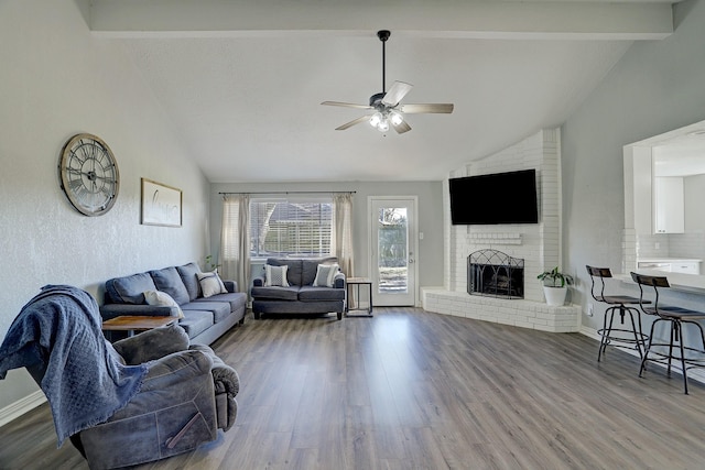 living room featuring vaulted ceiling with beams, ceiling fan, a brick fireplace, and hardwood / wood-style flooring