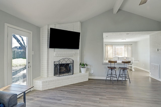 living room featuring vaulted ceiling with beams, wood-type flooring, and a brick fireplace