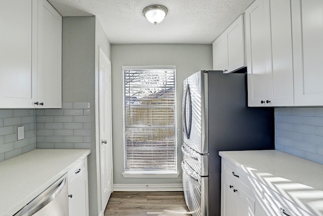 kitchen with stainless steel appliances, decorative backsplash, white cabinetry, and light hardwood / wood-style floors