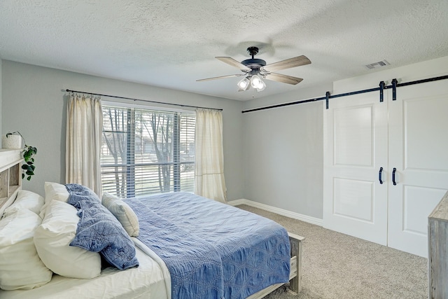 bedroom featuring carpet flooring, a textured ceiling, a barn door, and ceiling fan