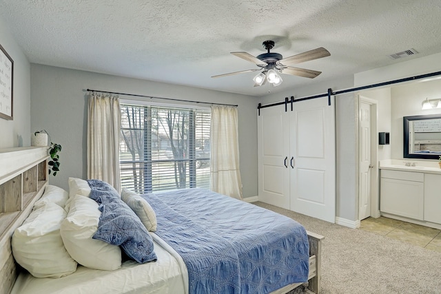 bedroom featuring light carpet, ensuite bathroom, ceiling fan, a barn door, and a textured ceiling