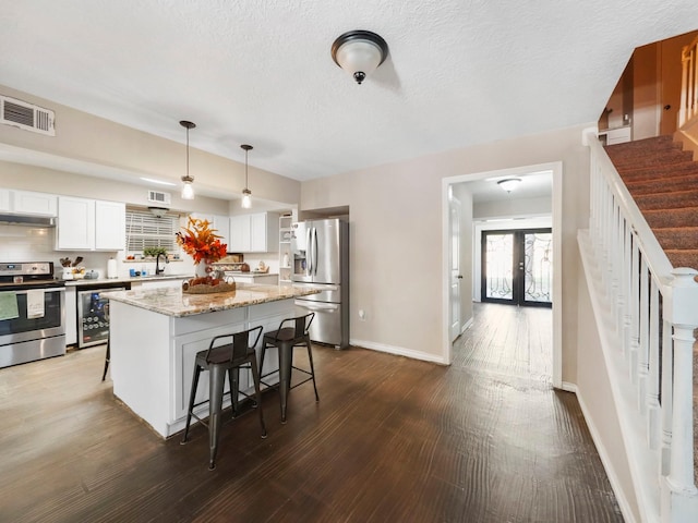 kitchen with a kitchen breakfast bar, stainless steel appliances, dark wood-type flooring, pendant lighting, and white cabinetry