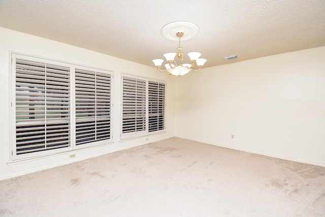 carpeted spare room featuring a notable chandelier and a textured ceiling