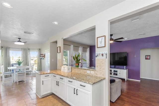 kitchen with kitchen peninsula, light stone countertops, white cabinets, and a textured ceiling