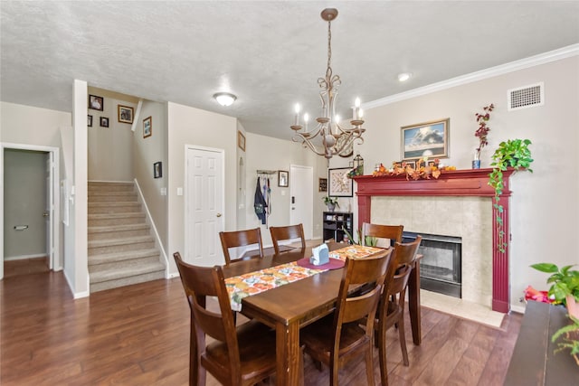 dining area featuring a tile fireplace, an inviting chandelier, dark hardwood / wood-style flooring, a textured ceiling, and ornamental molding