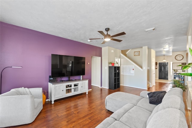 living room with a textured ceiling, ceiling fan, and dark wood-type flooring