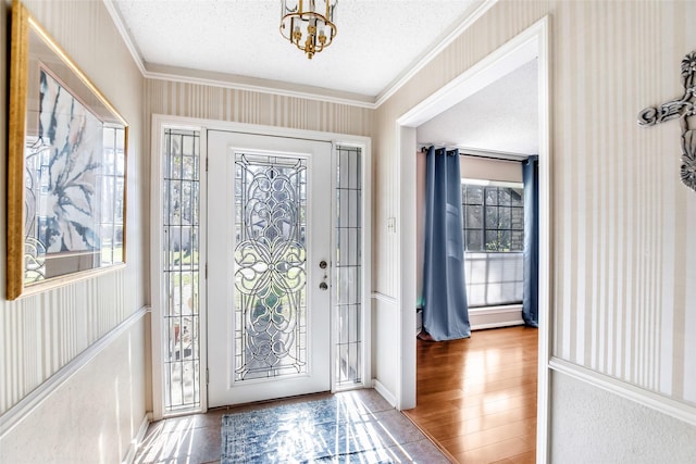 entryway with hardwood / wood-style flooring, crown molding, a textured ceiling, and a chandelier