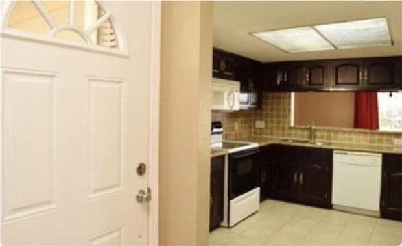 kitchen with sink, tasteful backsplash, white appliances, dark brown cabinets, and light tile patterned flooring