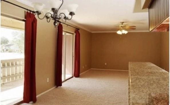 empty room with ceiling fan with notable chandelier, light colored carpet, and ornamental molding