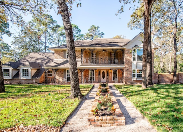 front facade featuring a balcony, ceiling fan, and a front lawn