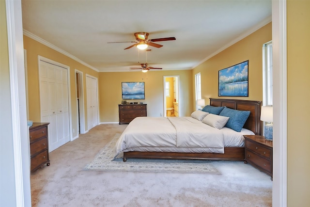 bedroom featuring two closets, ensuite bathroom, crown molding, ceiling fan, and light colored carpet