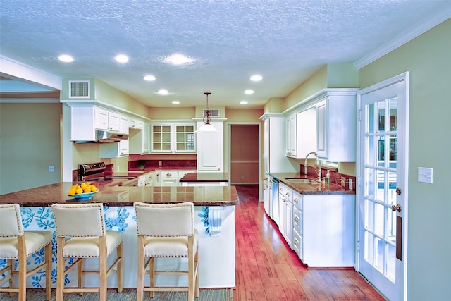 kitchen with white cabinets, sink, a textured ceiling, appliances with stainless steel finishes, and decorative light fixtures