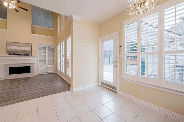 doorway to outside with a fireplace, light wood-type flooring, built in features, and ceiling fan with notable chandelier