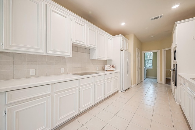 kitchen featuring black electric stovetop, backsplash, light tile patterned floors, white refrigerator, and white cabinets