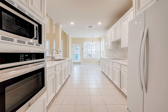 kitchen featuring appliances with stainless steel finishes, sink, light tile patterned floors, an inviting chandelier, and white cabinetry