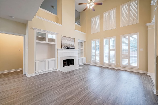 unfurnished living room featuring hardwood / wood-style floors, ceiling fan, built in shelves, a towering ceiling, and a fireplace