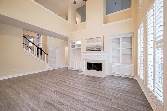 unfurnished living room with a fireplace, built in shelves, a towering ceiling, and hardwood / wood-style floors