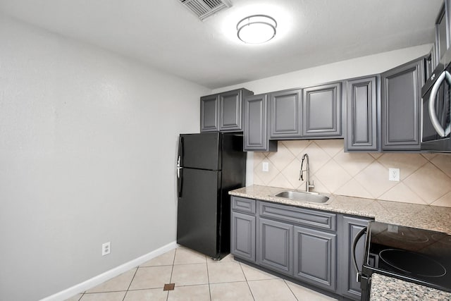 kitchen featuring decorative backsplash, black refrigerator, stove, and sink