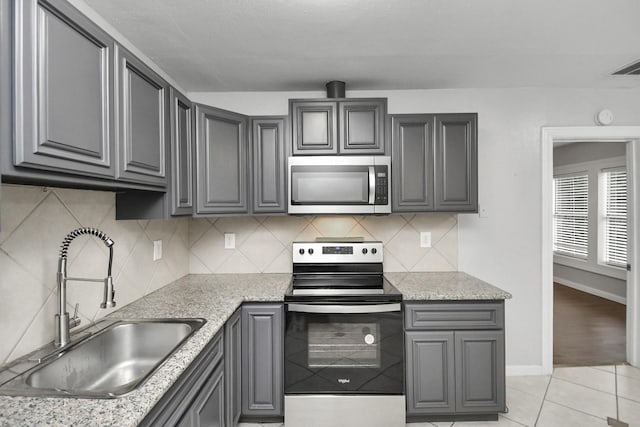 kitchen with light tile patterned flooring, stainless steel appliances, light stone countertops, and sink