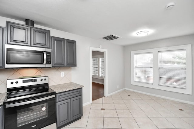 kitchen with backsplash, gray cabinets, light tile patterned floors, appliances with stainless steel finishes, and light stone counters