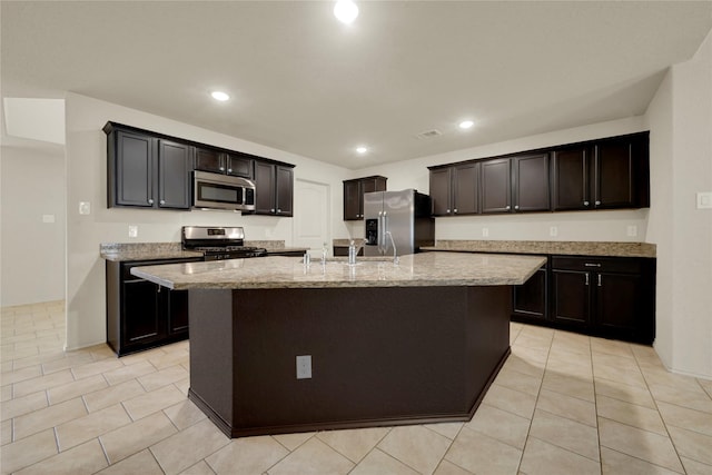 kitchen with light stone countertops, stainless steel appliances, sink, light tile patterned floors, and a center island with sink