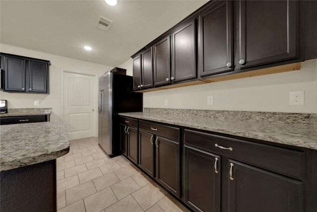 kitchen featuring light tile patterned floors, dark brown cabinetry, light stone counters, and stainless steel refrigerator