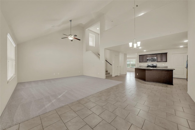 unfurnished living room featuring ceiling fan with notable chandelier, light colored carpet, and high vaulted ceiling