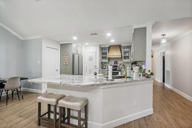 kitchen featuring sink, kitchen peninsula, stainless steel fridge, light hardwood / wood-style floors, and custom exhaust hood