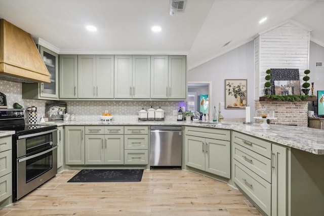 kitchen with custom exhaust hood, backsplash, vaulted ceiling, light wood-type flooring, and stainless steel appliances