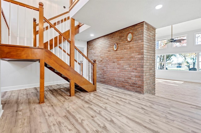 stairs featuring hardwood / wood-style floors, ceiling fan, and brick wall