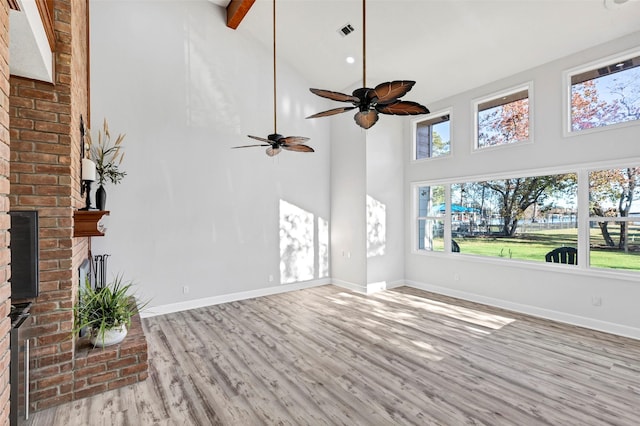 unfurnished living room featuring a wealth of natural light, a fireplace, high vaulted ceiling, and light wood-type flooring