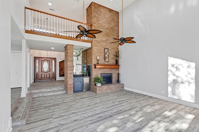 unfurnished living room with ceiling fan, a brick fireplace, light hardwood / wood-style flooring, decorative columns, and a towering ceiling