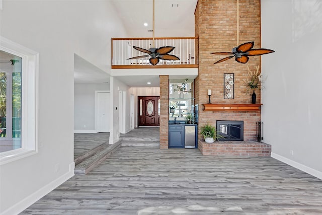 unfurnished living room with ceiling fan, light wood-type flooring, a towering ceiling, and a fireplace