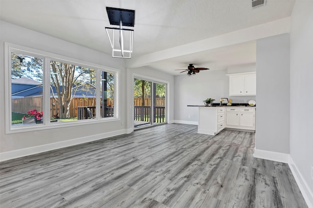 unfurnished living room with ceiling fan, plenty of natural light, a textured ceiling, and light hardwood / wood-style flooring