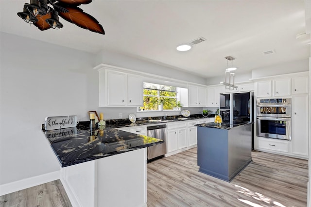 kitchen with appliances with stainless steel finishes, light hardwood / wood-style flooring, white cabinetry, and a kitchen island