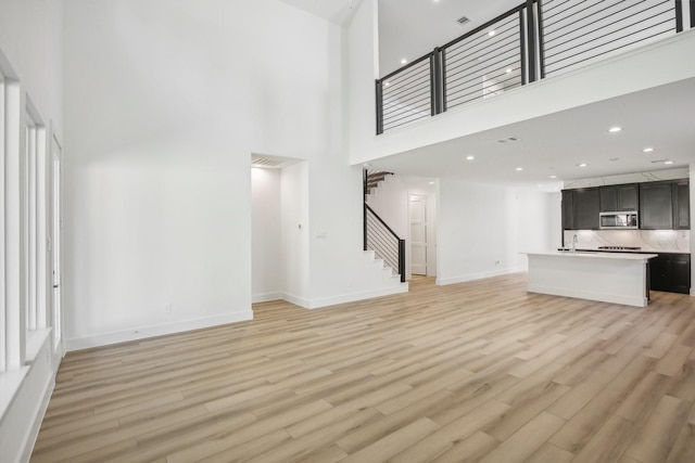 unfurnished living room with light wood-type flooring, a towering ceiling, and sink