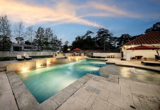 pool at dusk with pool water feature, exterior kitchen, and a patio