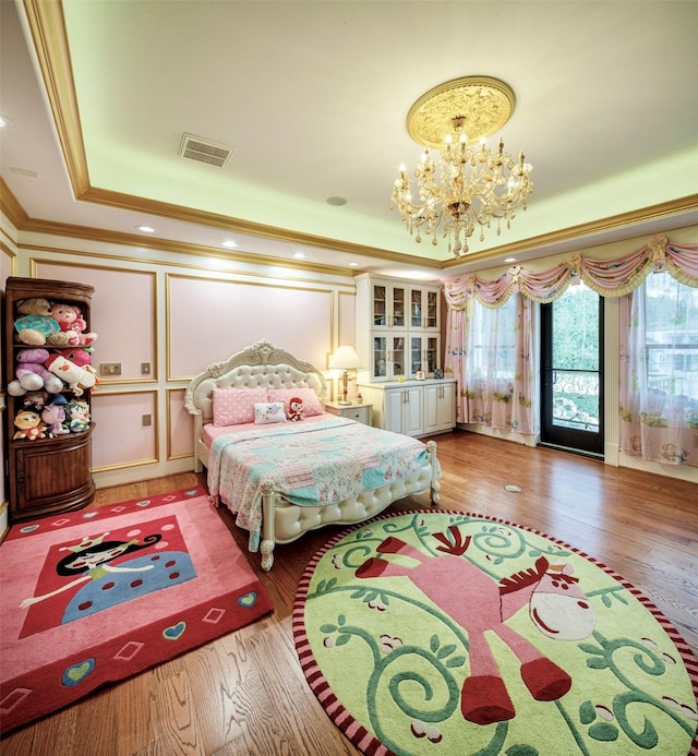 bedroom with hardwood / wood-style flooring, a notable chandelier, ornamental molding, and a tray ceiling