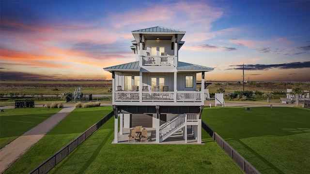 back house at dusk featuring a lawn and a balcony