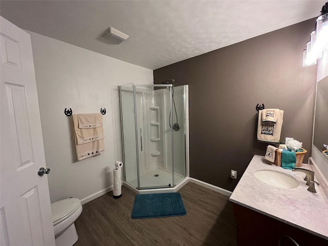 bathroom featuring vanity, wood-type flooring, a shower with shower door, and toilet