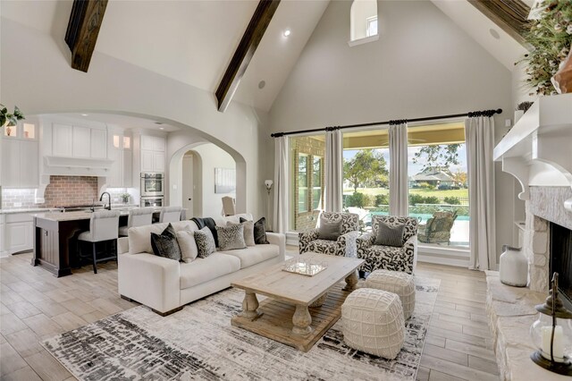 living room with a high end fireplace, beam ceiling, light wood-type flooring, and high vaulted ceiling