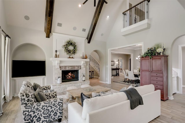 living room with beamed ceiling, light wood-type flooring, a fireplace, and high vaulted ceiling