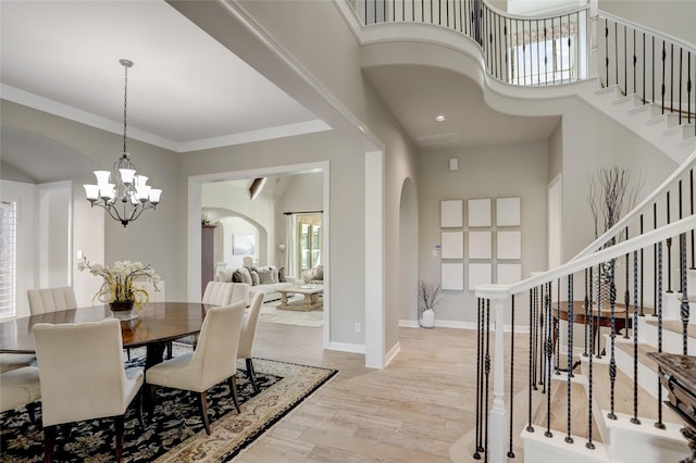 dining area featuring a notable chandelier, light wood-type flooring, ornamental molding, and a high ceiling