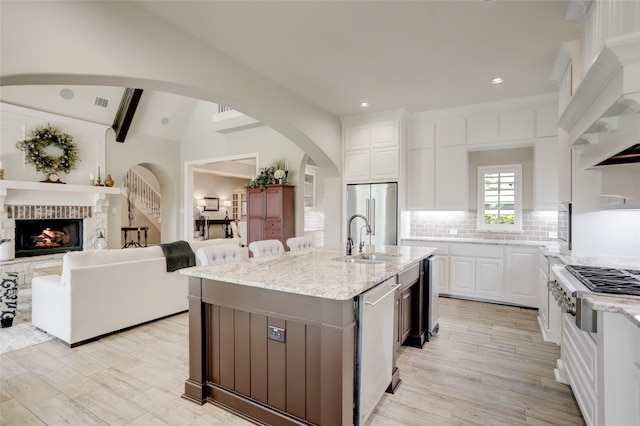 kitchen with a kitchen island with sink, white cabinets, vaulted ceiling with beams, appliances with stainless steel finishes, and light stone counters