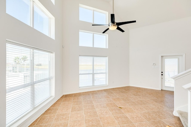 unfurnished living room featuring ceiling fan, a healthy amount of sunlight, and a high ceiling