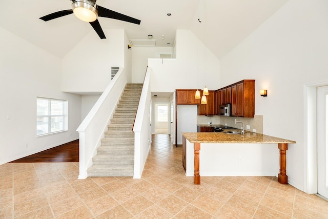 kitchen featuring kitchen peninsula, high vaulted ceiling, ceiling fan, and light stone counters