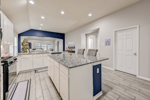 kitchen featuring a kitchen island, white cabinetry, kitchen peninsula, light stone counters, and stainless steel range with gas cooktop