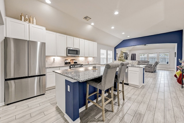 kitchen featuring vaulted ceiling, a center island, a breakfast bar, light stone countertops, and appliances with stainless steel finishes